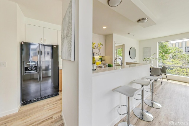 kitchen with white cabinetry, a healthy amount of sunlight, light hardwood / wood-style floors, and black refrigerator with ice dispenser