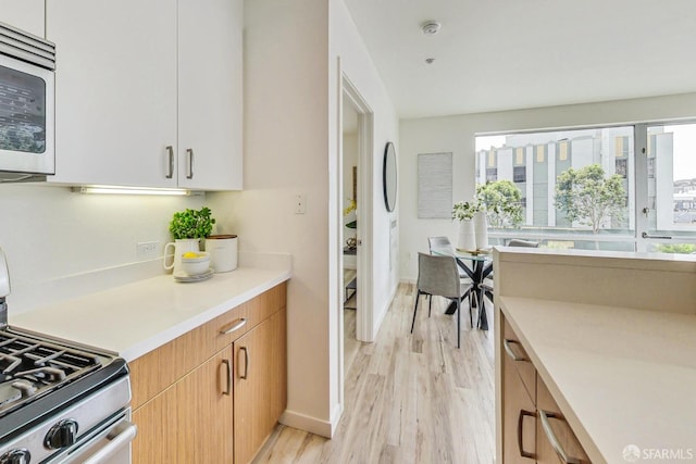 kitchen with stainless steel appliances, white cabinets, and light wood-type flooring