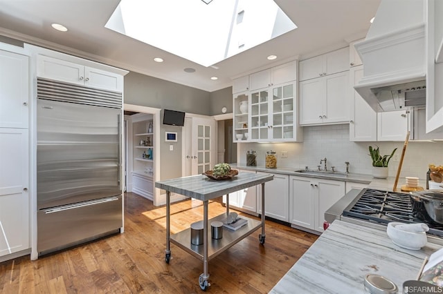 kitchen featuring a skylight, white cabinetry, sink, built in refrigerator, and light hardwood / wood-style flooring