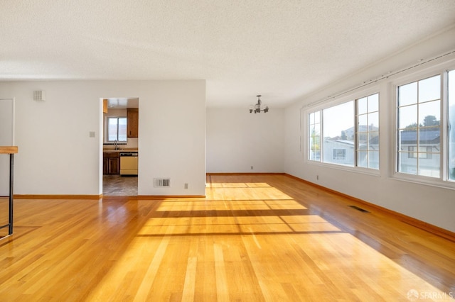 spare room with a textured ceiling, light hardwood / wood-style floors, sink, and an inviting chandelier