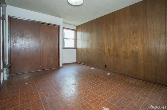 2567 Bryant St, San Francisco, CA 94110 - unfurnished bedroom featuring brick patterned floors, wooden walls, a closet, and a textured ceiling