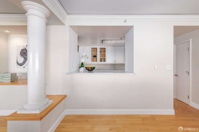 interior space featuring light wood-style floors, decorative columns, baseboards, and crown molding