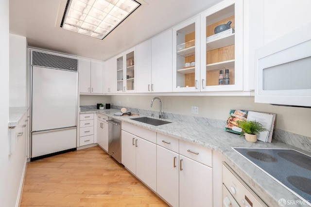 kitchen with paneled built in fridge, glass insert cabinets, white cabinets, and a sink