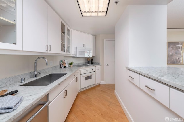 kitchen with light stone counters, white appliances, a sink, white cabinetry, and glass insert cabinets