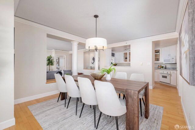 dining space with ornate columns, light wood-style flooring, ornamental molding, and baseboards