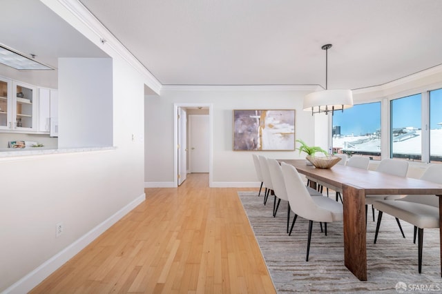 dining area with ornamental molding, light wood-type flooring, a notable chandelier, and baseboards