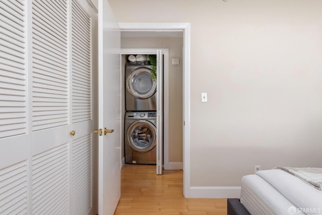 laundry room featuring laundry area, light wood-style flooring, stacked washer and clothes dryer, and baseboards