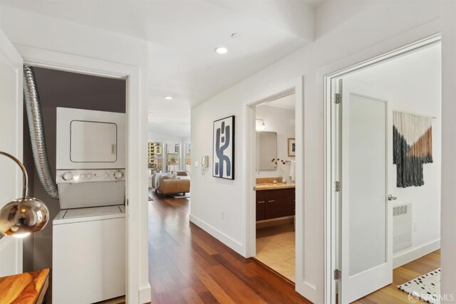 washroom featuring stacked washing machine and dryer, wood finished floors, baseboards, and recessed lighting