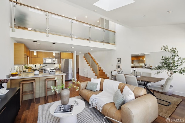 living area with dark wood-style flooring, a towering ceiling, a skylight, baseboards, and stairway