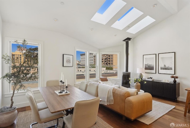 dining room featuring a skylight, vaulted ceiling, a wood stove, wood finished floors, and plenty of natural light