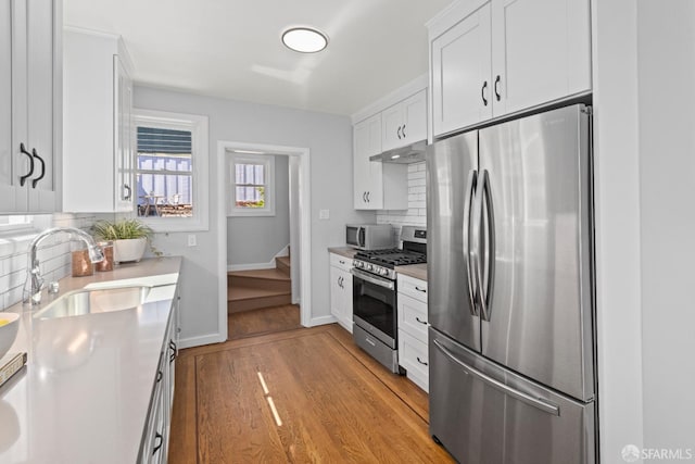 939 Innes Ave, San Francisco, CA 94124 - kitchen with appliances with stainless steel finishes, under cabinet range hood, tasteful backsplash, white cabinets, and light wood-type flooring