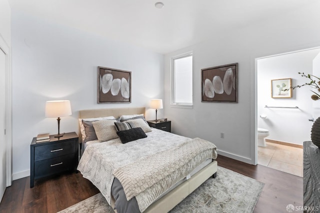 bedroom with ensuite bathroom, dark wood-type flooring, and baseboards