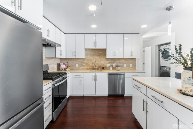 kitchen with stacked washing maching and dryer, a sink, light countertops, under cabinet range hood, and appliances with stainless steel finishes