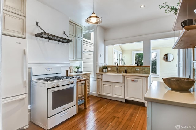 kitchen with sink, white appliances, hardwood / wood-style flooring, hanging light fixtures, and tasteful backsplash