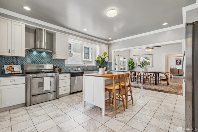 882 56th St, Oakland, CA 94608 - kitchen featuring appliances with stainless steel finishes, wall chimney exhaust hood, light marble finish floors, a kitchen breakfast bar, and decorative backsplash
