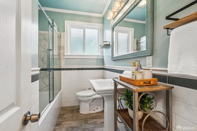 882 56th St, Oakland, CA 94608 - bathroom featuring ornamental molding, wood finished floors, bath / shower combo with glass door, tile walls, and wainscoting