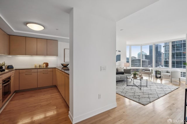 kitchen with light brown cabinetry, gas stovetop, light hardwood / wood-style flooring, a wall of windows, and oven