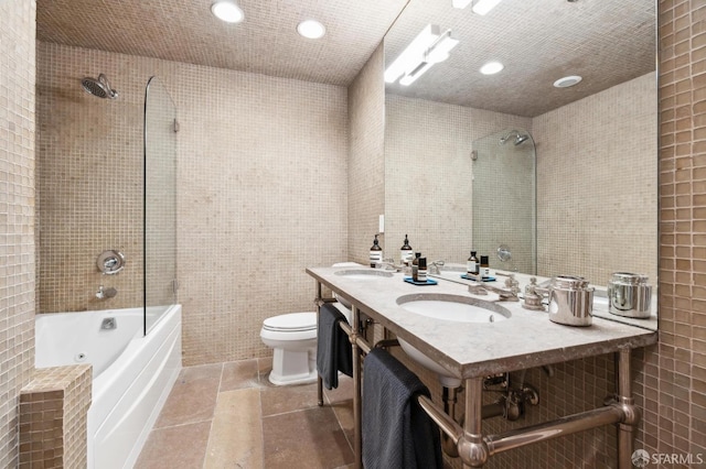 bathroom with tiled shower / bath, toilet, tile walls, and double sink