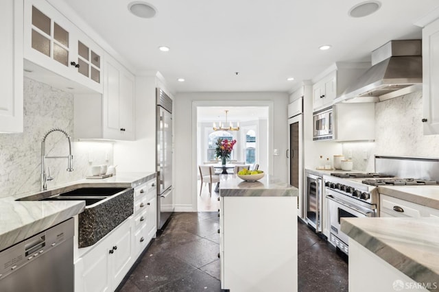 kitchen featuring built in appliances, wall chimney range hood, white cabinetry, and sink