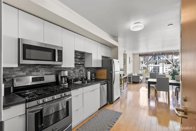 kitchen with appliances with stainless steel finishes, decorative backsplash, light hardwood / wood-style floors, white cabinets, and sink