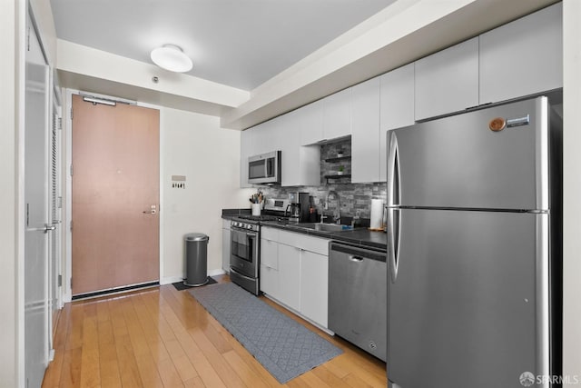 kitchen with light hardwood / wood-style floors, sink, white cabinets, decorative backsplash, and stainless steel appliances