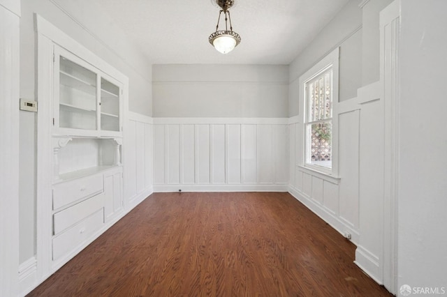 unfurnished room featuring dark wood finished floors, a decorative wall, built in features, and wainscoting