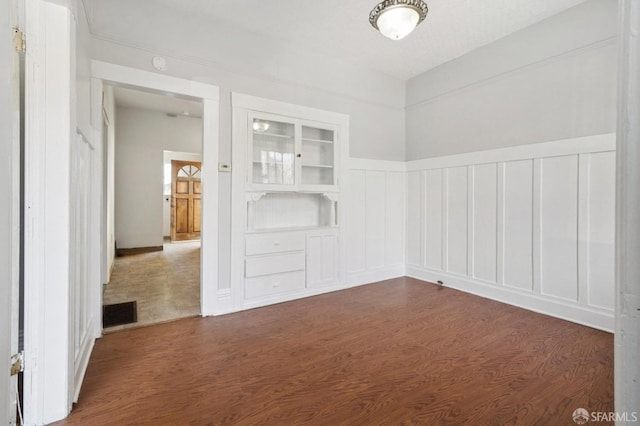 empty room featuring visible vents, built in shelves, dark wood-type flooring, and a decorative wall