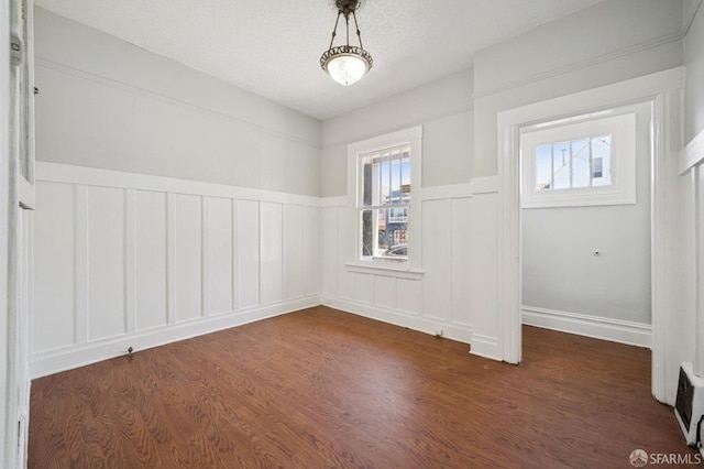 empty room with dark wood-type flooring and wainscoting