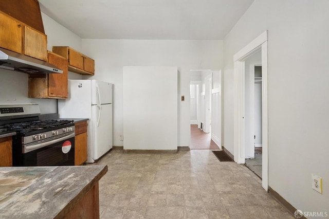 kitchen featuring baseboards, under cabinet range hood, brown cabinets, freestanding refrigerator, and gas stove