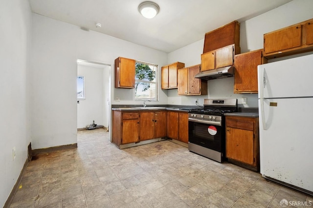 kitchen with dark countertops, under cabinet range hood, freestanding refrigerator, brown cabinetry, and gas stove