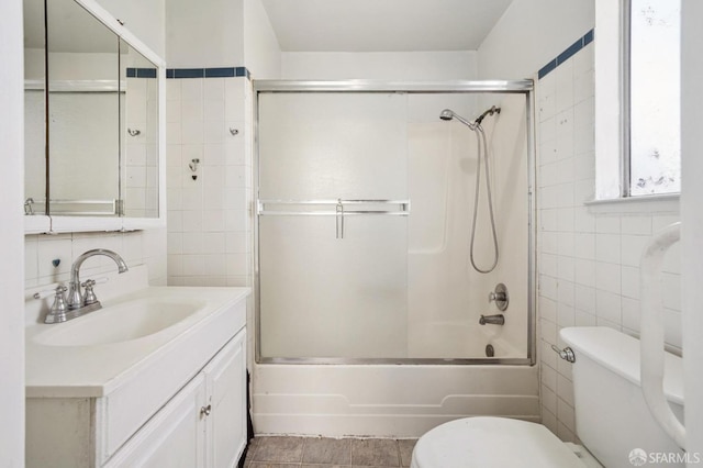 full bath with vanity, toilet, tile walls, and shower / bath combination with glass door