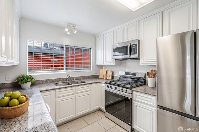 kitchen featuring a sink, stainless steel appliances, light tile patterned flooring, light stone counters, and white cabinetry