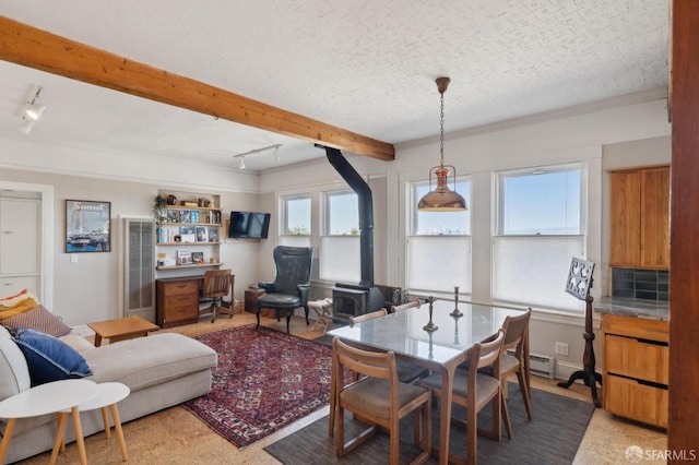 dining room with track lighting, beamed ceiling, a wood stove, and a textured ceiling