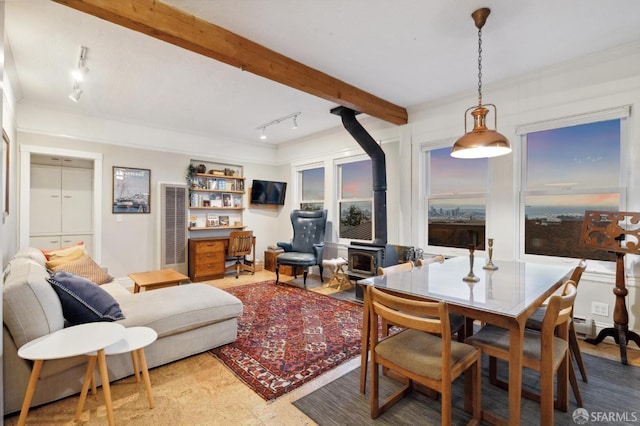 dining area featuring rail lighting, beam ceiling, and a wood stove