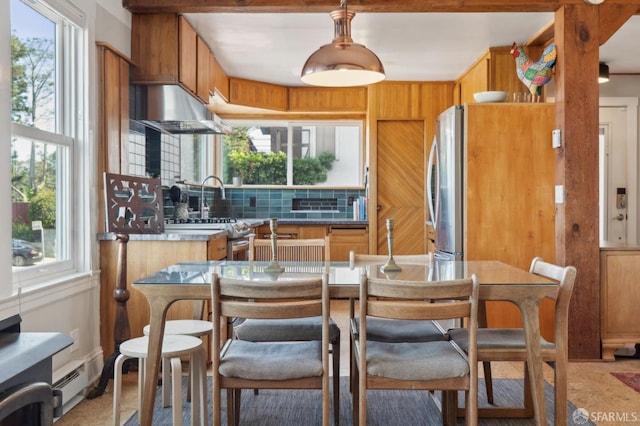 kitchen with under cabinet range hood, baseboard heating, tasteful backsplash, and brown cabinetry