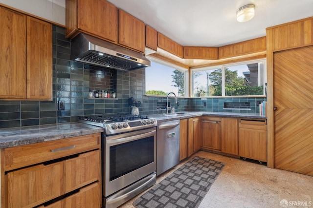 kitchen featuring tasteful backsplash, under cabinet range hood, brown cabinets, stainless steel appliances, and a sink