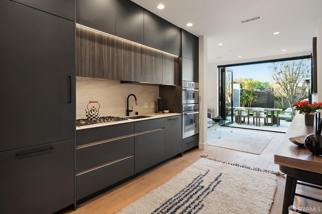 kitchen with stainless steel appliances, tasteful backsplash, sink, and light hardwood / wood-style flooring