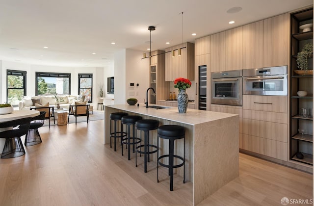 kitchen with a kitchen island with sink, light brown cabinetry, and oven