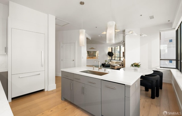 kitchen featuring gray cabinetry, a center island with sink, pendant lighting, and sink