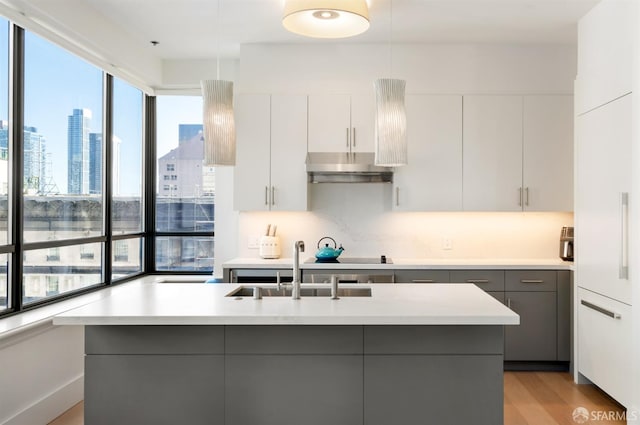 kitchen featuring decorative light fixtures, white cabinetry, gray cabinetry, and an island with sink