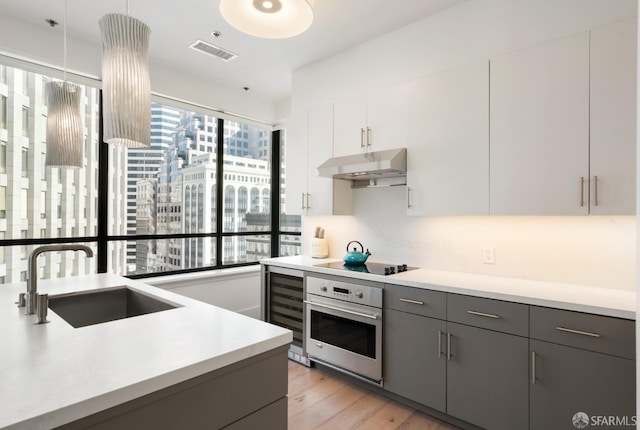 kitchen with oven, pendant lighting, sink, white cabinetry, and black electric cooktop