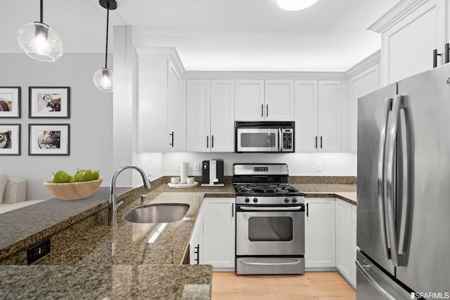 kitchen featuring white cabinetry, sink, hanging light fixtures, stainless steel appliances, and light wood-type flooring