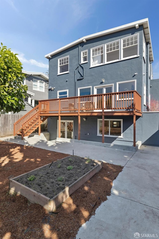 rear view of property with stucco siding, fence, a garden, a wooden deck, and stairs