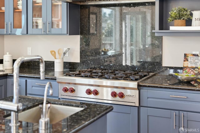 kitchen featuring luxury stove, a sink, dark stone counters, tasteful backsplash, and glass insert cabinets