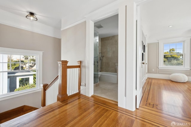 hall featuring light wood-type flooring, plenty of natural light, visible vents, and an upstairs landing