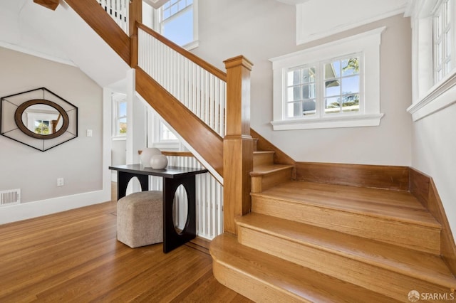 staircase featuring a healthy amount of sunlight, a towering ceiling, baseboards, and wood finished floors