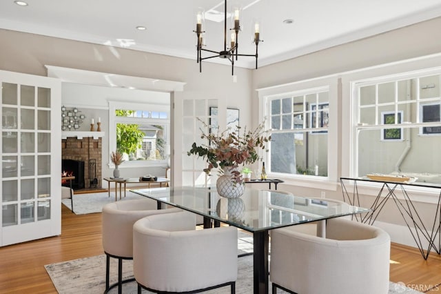 dining area featuring crown molding, recessed lighting, an inviting chandelier, a brick fireplace, and wood finished floors