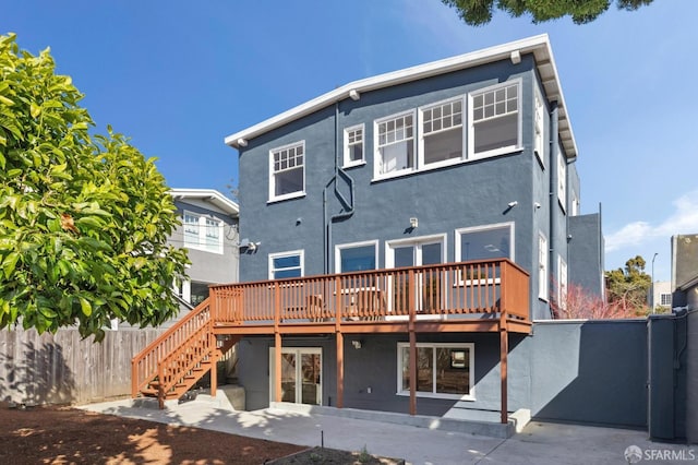 rear view of property featuring stucco siding, fence, a wooden deck, and stairs