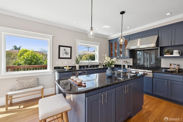 kitchen featuring an island with sink, light wood-style flooring, ornamental molding, glass insert cabinets, and extractor fan