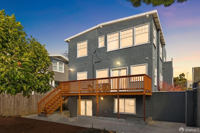 back of property at dusk featuring fence, stairway, a wooden deck, stucco siding, and a patio area